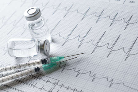medical ampules and syringe on EKG graph background