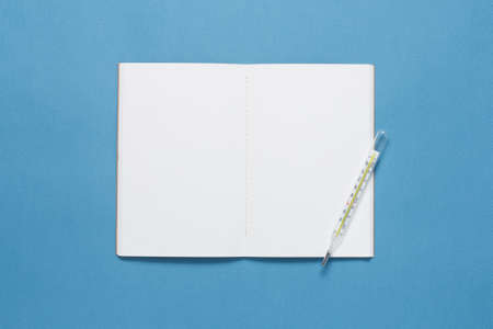 Notebook and thermometer on blue backgroundの写真素材