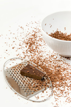 The pieces of chocolate lying in the white bowl prepared to be gratedの写真素材