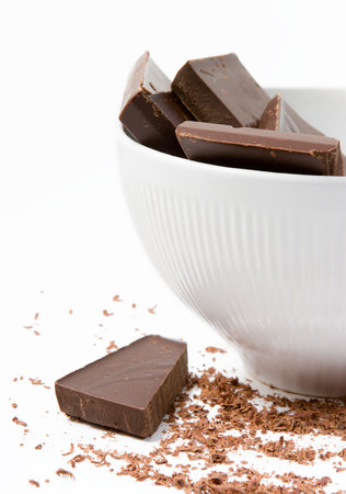 Pieces of dark chocolate in the white bowl with the chocolate shavings lying aroundの写真素材