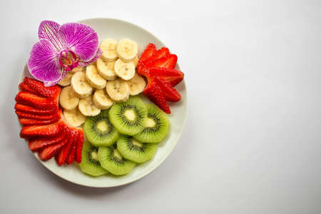 Fruit plate with strawberries, bananas and kiwi decorated with orchid flower. On a white background. Flat lay. Top view. Place for text.の写真素材