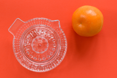 Glass manual juicer and a single orange isolated on a bright orange background.の写真素材
