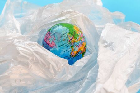 Concept of the plastic pollution problem in the world.  The planet earth is floating around in a soup of white plastic bags on against blue background.の写真素材