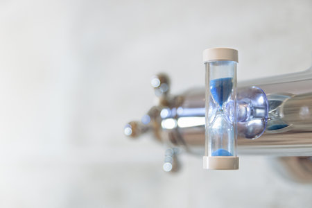 A shower faucet in the bathroom with an hourglass attached to cut back shower time in order to save water and energy.の写真素材