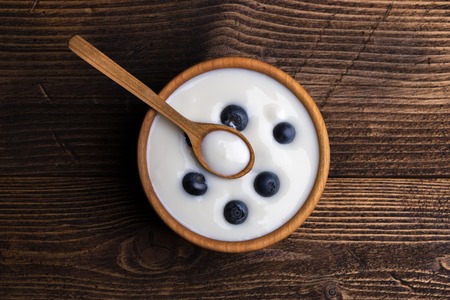 White yogurt in natural wooden bowl with blueberries. Top view on rustic background.の写真素材