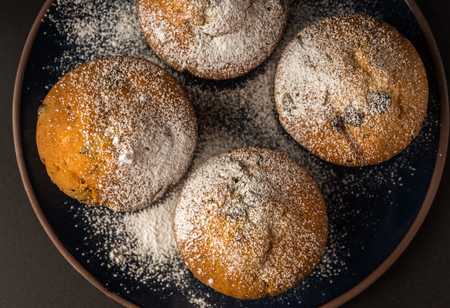 Chocolate muffins with powdered sugar on dark blue plate.の写真素材