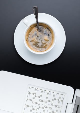 White cup of coffe on dark background with laptop. Top view.の写真素材