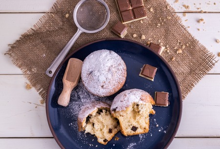 Muffins powdered by sugar on blue plate and white wooden background.
