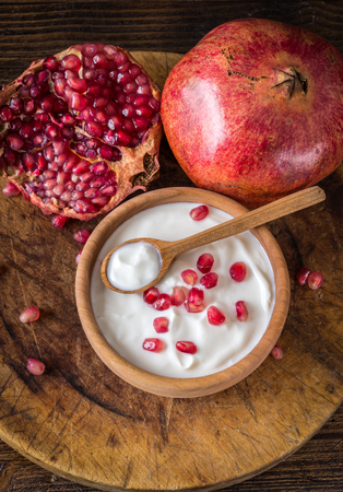 White yogurt with pomegranates in wooden bowl on rustic table. Top view.の写真素材
