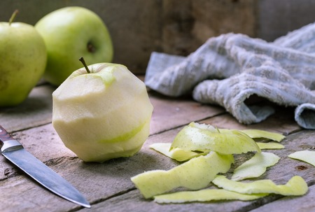 Green peeled apple on wooden desk with knife and apples behind.の写真素材