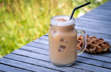 Ice coffee in glass mug with milk and cinnamon on wooden table in the garden.の写真素材