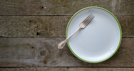 Empty white plate with fork on natural wooden desk.の写真素材