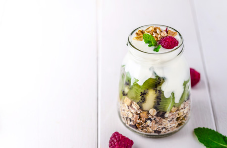 White yogurt with muesli in glass bowl with pieces of kiwi on the top.の写真素材