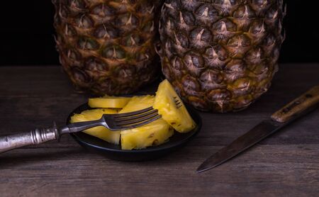 Sliced pineapple on old rustic desk with knife and with whole pineapple behind. Black background.の写真素材