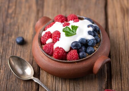Granola with white yogurt with raspberries and blueberries in ceramic bowl on natural wooden desk.の写真素材