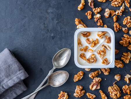 White yogurt in plastic square cup with walnuts with spoons on gray background. Flat view.の写真素材