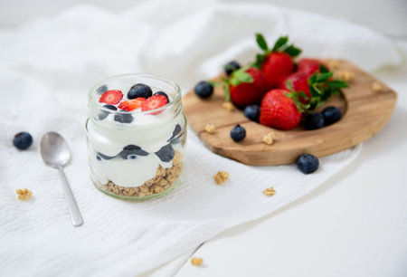 White yogurt in glass bowl with blueberries and strawberries and oatmeal on white background.の写真素材