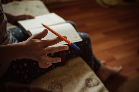 A girl with a notebook twirls a pen with her fingers while sitting on the couch at homeの写真素材