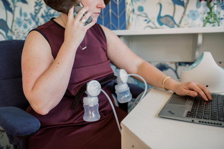 Woman on mobile phone and laptop while pumping at desk.の写真素材