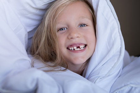 little girl without front teeth smiling in the morning in bedの写真素材