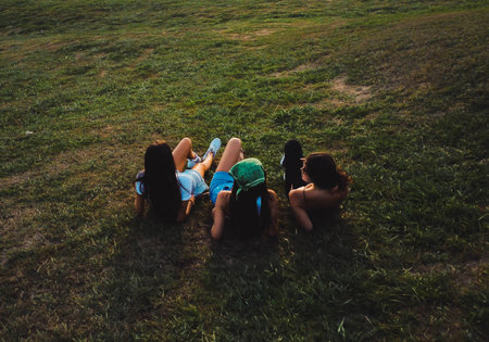three women sitting on the grass against sea landscape with sunsetの写真素材