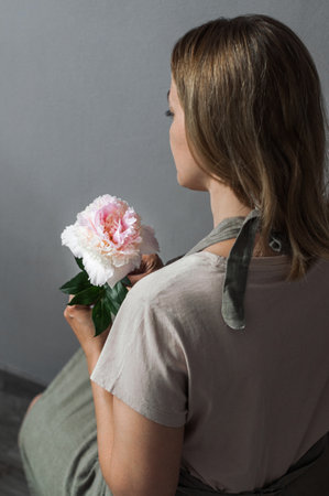 A girl with a peony in her hands in a linen apron, half-turned.の写真素材