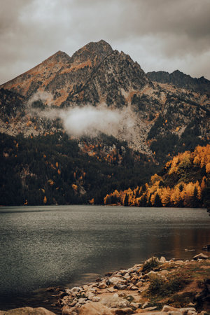 Mountain next to a lake and some trees during a cloudy dayの写真素材