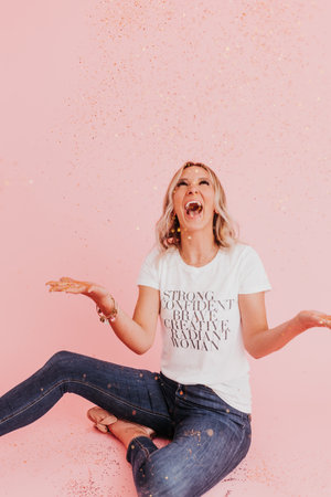 Woman sits on floor laughing after throwing gold glitterの写真素材