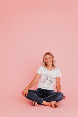 Young female sits against pink studio backdrop looking at cameraの写真素材