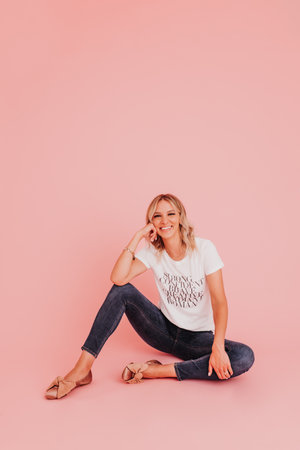 Young female sits against pink studio backdrop looking at cameraの写真素材