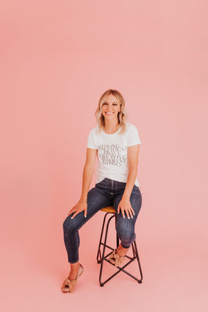 Female sits confidently on stool against pink studio backdropの写真素材