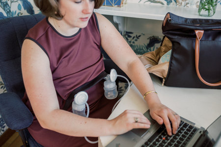 Caucasian mother pumps while working on laptop at desk.の写真素材