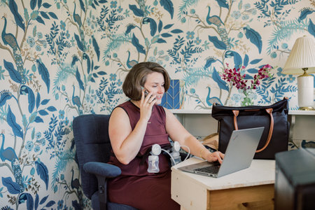 Caucasian mom at desk talks on phone while using breast pump.の写真素材