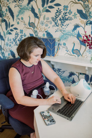 Caucasian mother pumps while sitting at desk at work.の写真素材