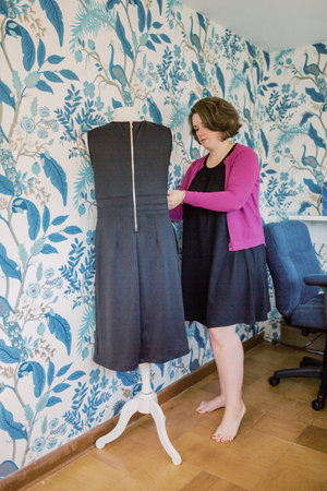 Female adjusts black dress on bust in blue wallpaper room.の写真素材