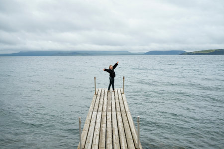 Cheerful girl standing on quay spreading armsの写真素材