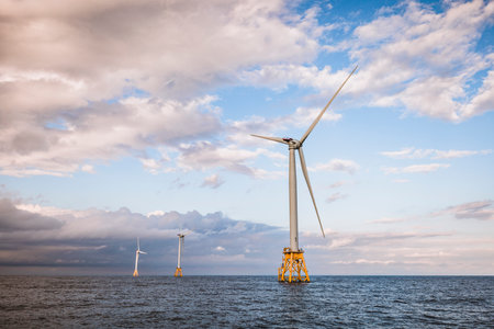 three wind turbines off shore with clouds in middle of oceanの写真素材