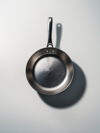 A reflective stainless steel frying pan cast in soft light, showcasing its sleek design and subtle scratches.の素材