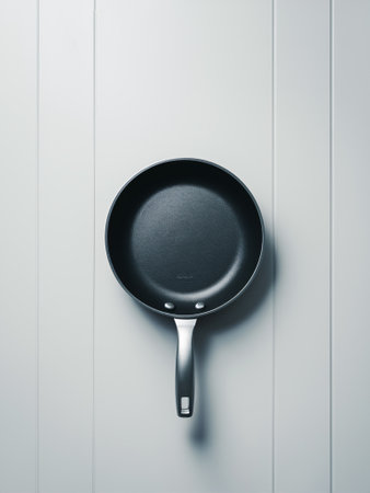 Minimalist view of a sleek black frying pan against a pale wall, showcasing modern kitchen aesthetics.の素材