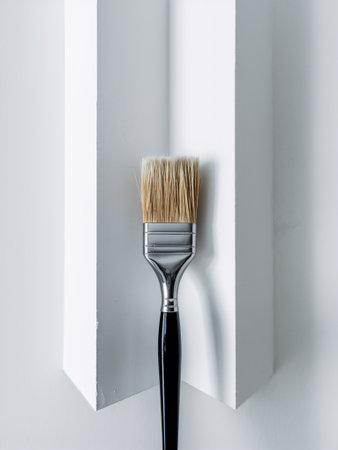 A close-up of a paintbrush resting against a pristine white wall, symbolizing creativity and DIY projects.の素材