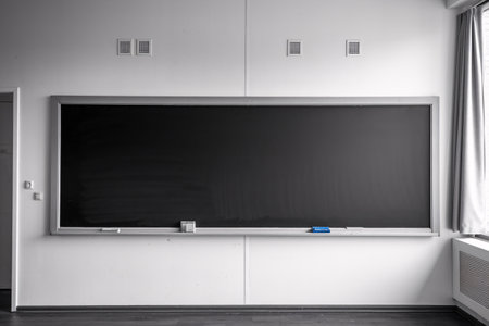 A clean, empty blackboard in a bright classroom setting, ideal for teaching and learning.の素材