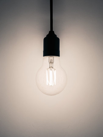 A minimalistic hanging light bulb illuminating a plain wall, creating a serene, warm atmosphere.の素材