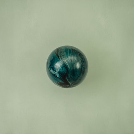 A mesmerizing teal and black marble ball set against a soft green background.の素材