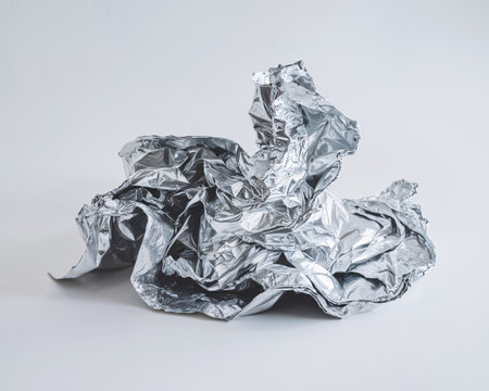 Crumpled metallic foil against a soft gray backdrop, showcasing intricate textures and reflections.の素材