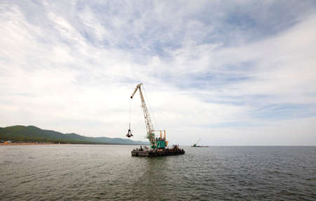 A floating crane at sea loads a barge with sandの写真素材