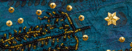 Close up detail of vintage sari fabric with gold and black embellishments.Blue background.