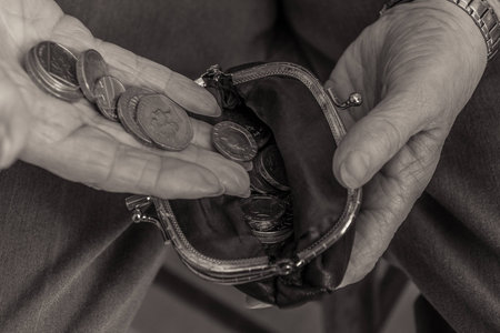 British pensioner putting coins into a purse. Close up of hands. Black and white image. Cost of...