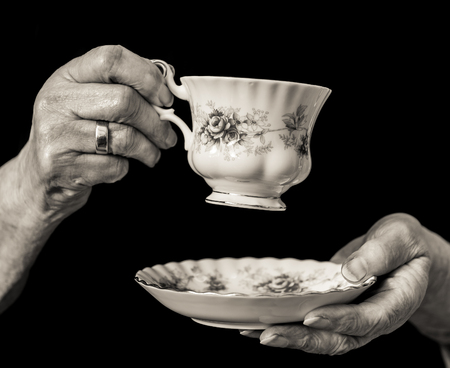 Traditional China teacup and saucer held in an elderly English woman's hands about to take a drink of tea. Black and white image.の写真素材