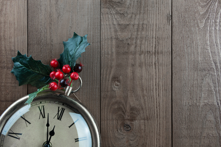 Christmas vintage clock with Holly berries on a wood background. Part of clock showing. Time almost 12 o'clock, almost Christmas! Vintage, traditional muted neutral brown colors with bright red berries. Lots of copy space.の写真素材