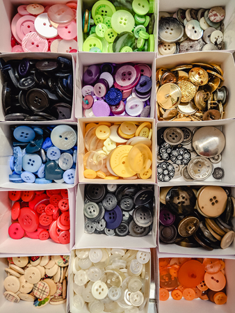 Assortment of buttons in individual boxes, sorted into a rainbow of colours. Viewed from above.